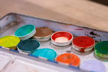 Closeup of an Used colorful make up palette with a lot of eye shadows. Green, blue, navy, yellow, orange, sparkly blue. Grease paint. Stage makeup workshop banner. Selective focus.