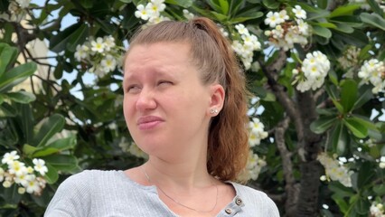 young woman suffering from pollen allergy at summer day in front of flowers