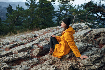 Woman in yellow raincoat checking phone while enjoying mountain view during travel trip