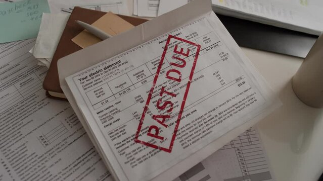 Close-up shot of unpaid electricity bill with large red stamp, tax return forms, on table in home of unemployed or bankrupt person, struggling to afford household expenses