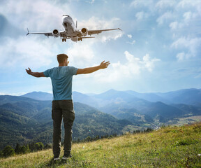 Man looking at airplane flying in sky over mountains, back view