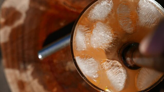 POV of a person mixing a Caipirinha with a wooden muddler and then placing a drinking straw into the glass. Close-up of a Brazilian Caipirinha glass on the table: tangerine, cacha&ccedil;a, sugar, and ice.