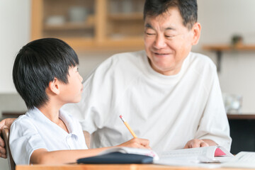 Obraz premium 家のダイニングで孫の宿題を教える高齢者男性と小学生の子供 