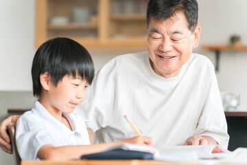 家のダイニングで孫の宿題を教える高齢者男性と小学生の子供
