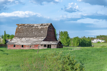 Vintage deteriorating and falling apart barn and a modern house in the background © Gelu Popa