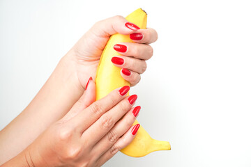 Hands of a woman with bright red nail polish holding large curvy banana fruit isolated on white...