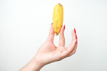 Hands of a woman with bright red nail polish holding small sized banana fruit isolated on white...
