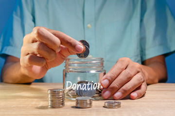 Hand putting coins into a glass jar. Donation and charity concept.