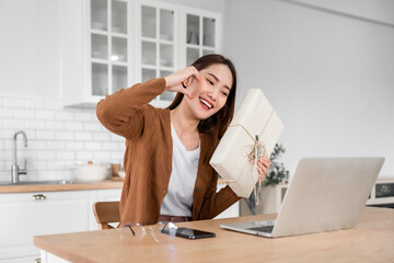 Young asian woman using computer laptop at home. Female showing gift box while on video conversation with friend. Happy birthday, Happy new year, Thanksgiving