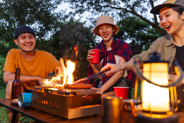Happy asian diverse group friends enjoy drinking a beer together. They feeling relaxed and refreshing while camping in the nature at night. Recreation and journey outdoor activity lifestyle.