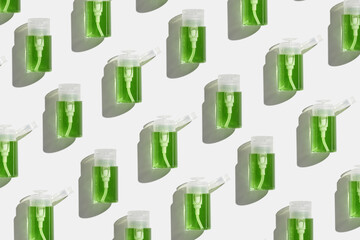 Transparent Pump dispensers with green colored liquid as pattern. Skincare essentials, spa beauty products on light background, Cosmetic bottles at sunlight, minimal top view geometric lauout