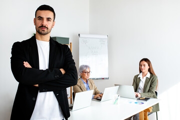 Portrait of young businessman looking at camera with serious expression and arms crossed standing in the office.