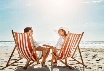 Couple, relax and sunshine on beach chair for vacation adventure, love and support of partner in summer journey. Happy, woman and man holding hands with ocean freedom, trust and travel in Bali island