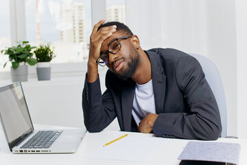 Stressed businessman in office suit sitting at desk with head in hands surrounded by papers and...
