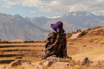 Woman with hat sitting in front of the mountain of Moray in Cusco