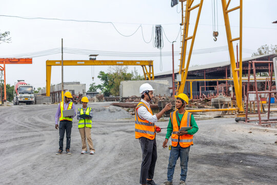 Factory engineers from different cultures in safety uniform using laptop computer and tablet to work together in a construction site