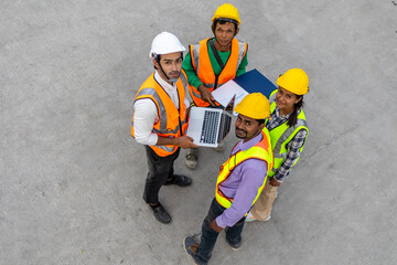 Top view of a group of civil engineers discussing their plan using computer application in a factory