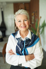 Fototapeta premium Portrait of confident happy successful senior businesswoman in elegant white blouse and silk scarf around neck standing with crossed hands and cheerful smile motivating you to run your own business