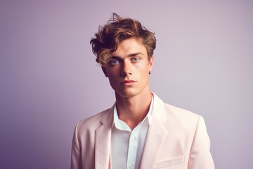A man in a pink suit and white shirt is standing in front of a purple background