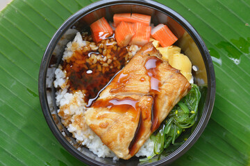 the close-up image of the Japanese dish featuring grilled Norwegian mackerel (saba) on rice and on green leaves background 