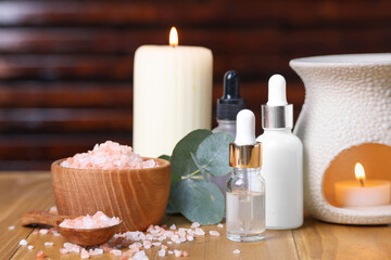 Different aromatherapy products, burning candles and eucalyptus leaves on wooden table, closeup