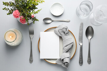 Empty menu, tableware, candle and floral decor on light grey table, flat lay. Mockup for design