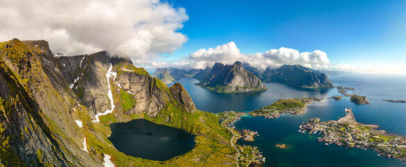 Panoramic view from a Norwegian mountaintop, featuring a winding fjord, a quaint village, and stunning mountains and sea vistas. Reinebringen hike Lofoten Norway