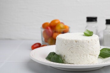 Fresh ricotta (cream cheese) and basil on light tiled table, closeup. Space for text