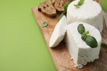 Fresh ricotta (cream cheese), basil, bread and knife on green table, closeup. Space for text