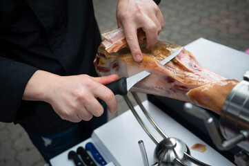 Close-up of hands preparing slices of Iberian ham with a knife at an outdoor festival