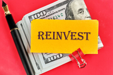 Business concept. Copy space. REINVEST text on a yellow piece of paper on dollars on a red background