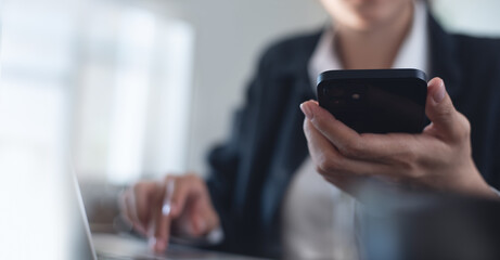 Business woman using mobile phone during working on laptop computer, surfing the internet, searching business data at modern office. Asian businesswoman online working on computer at workplace