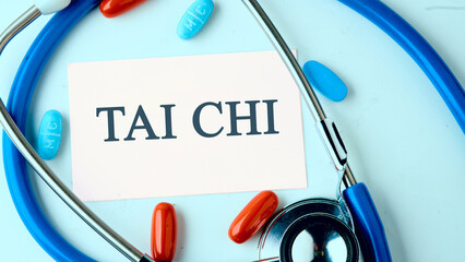 Sports and signal. Sign tai chi on a white business card on a blue background with a stethoscope, pills in a composition in cold tones