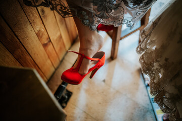 A bride in her wedding dress, seated gracefully, wearing striking red heels that add a bold touch...