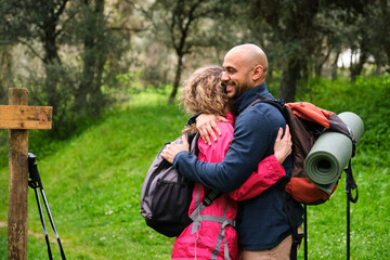 A man and woman hug each other while carrying backpacks after hiking. They are happy and love each...