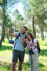Fototapeta premium A man and a woman are taking a selfie with apples during a hike. They are both smiling and seem to be enjoying their time together