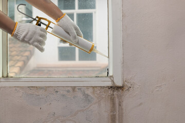 Construction worker using silicone sealant caulk for repair leaked inside window frame.