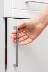 housewife opens a white kitchen cabinet. woman's hand opens the kitchen cabinet by the handle. vertical photo