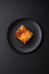 Delicious baked lasagna pasta with meat, sauce, salt, spices and herbs on a dark concrete background