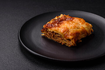 Delicious baked lasagna pasta with meat, sauce, salt, spices and herbs on a dark concrete background