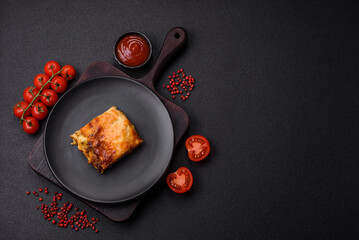Delicious baked lasagna pasta with meat, sauce, salt, spices and herbs on a dark concrete background