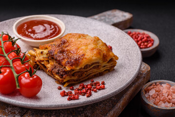 Delicious baked lasagna pasta with meat, sauce, salt, spices and herbs on a dark concrete background