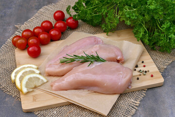 Fresh chicken breast on wooden board with tomatoes and lemon slices. © Racamani