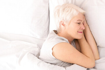 A woman is lying down in bed, covered by crisp white sheets. She appears relaxed and comfortable,...