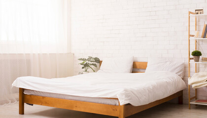 A bed is positioned next to a window in a bedroom. The room is illuminated by natural light filtering through the window. The bed is made with clean linens and pillows