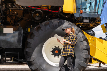 Woman agricultural farmer stands next to combine harvester and using her digital tablet.