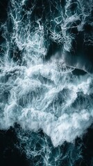 Naklejka premium Aerial view of crashing ocean waves creating dramatic white foam patterns against deep blue water, evoking a sense of power and natural beauty.