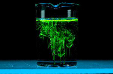 Dissolution and spread of a green substance in a flask with a clear liquid.