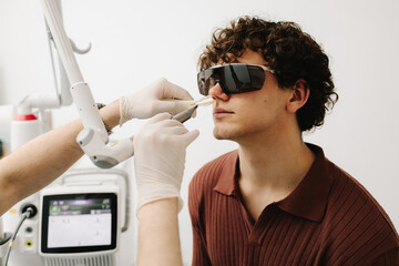 ENT doctor with laser treats man patient in protective glasses. Laser treatment inflammation of the...