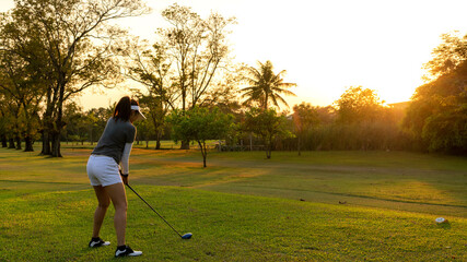 Fototapeta premium Golfer women sport course golf ball fairway. People lifestyle woman playing game golf swing tee of on the green grass sunset background. Asian female player game shot in summer. copy space for text